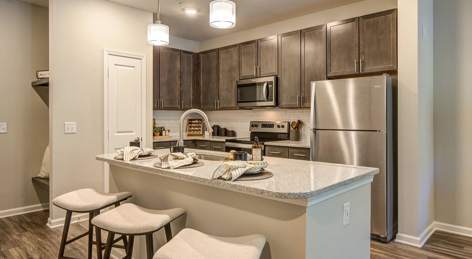 Modern kitchen featuring dark cabinets, stainless steel appliances, and a granite countertop with two stools. Warm and inviting ambiance.