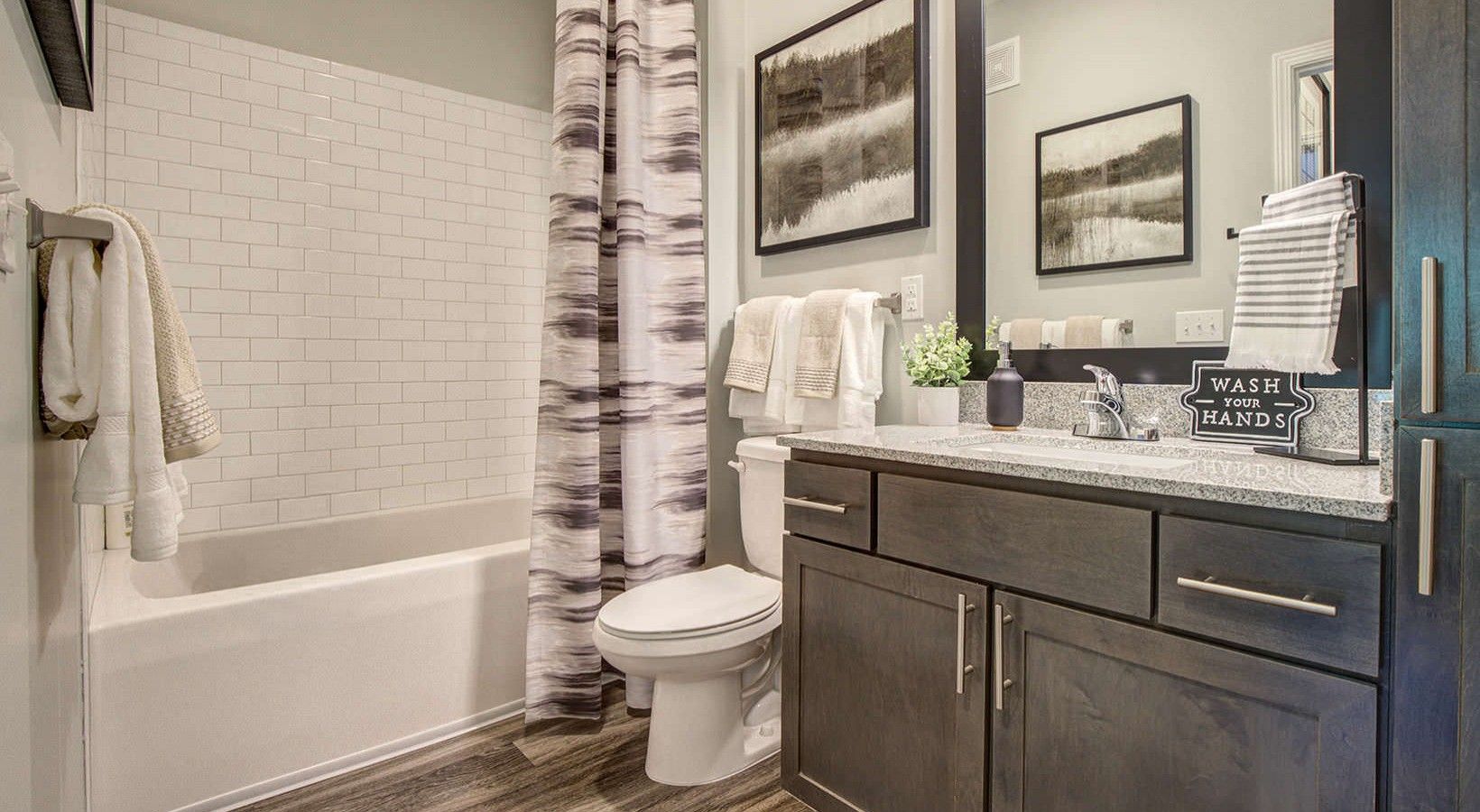 Modern bathroom featuring a white tiled shower, dark wood vanity, and decorative towels, complemented by a "Wash Your Hands" sign.
